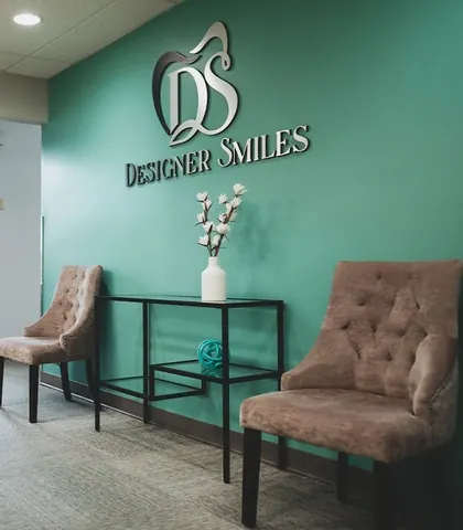 Designer Smiles reception: the DS logo on a teal wall above two tufted chairs.