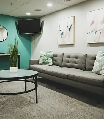 The waiting lounge, with a grey sofa, a round glass table and a wall TV.